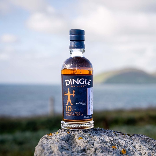 Dingle Distillery 10 Year Old Single Malt with a dark blue label and gold and white text sat on a rock with a scenic background.